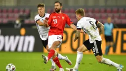 Pemain Swiss Admir Mehmedi (tengah) menendang bola melewati pemain Jerman Toni Kroos (kanan) pada pertandingan UEFA Nations League di Cologne, Jerman, Selasa (13/10/2020). Pertandingan berakhir dengan skor 3-3. (AP Photo/Martin Meissner)