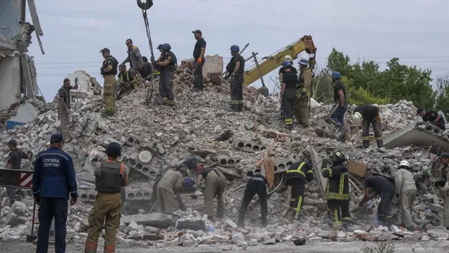 Petugas penyelamat berdiri di atas puing-puing di tempat kejadian setelah serangan rudal Rusia mengenai blok apartemen perumahan, di Chasiv Yar, wilayah Donetsk, Ukraina timur, Minggu, 10 Juli 2022. (AP Photo/Nariman El-Mofty)