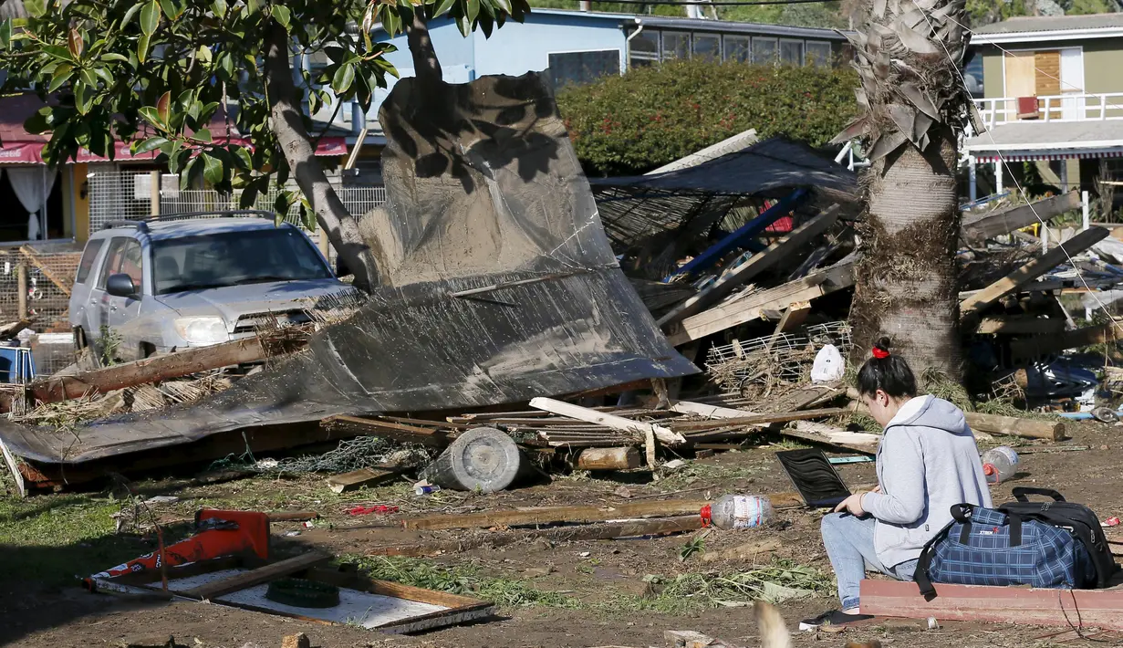 Seorang wanita menggunakan laptop di sebelah toko yang hancur usai gempa melanda kota Concon Chile (17/9/2015). Gempa yang menewaskan sekitar sepuluh orang dan memaksa satu juta orang mengungsi dari rumah mereka ke dekat pantai. (REUTERS/Rodrigo Garrido)