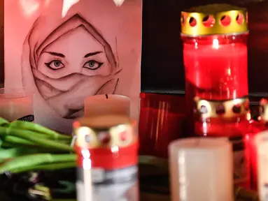 Gambar seorang wanita terlihat di antara lilin dan bunga saat berkabung untuk para korban penembakan brutal di Hanau, Jerman, Kamis (20/2/2020). Penembakan yang terjadi di dua bar shisha Kota Hanau menewaskan sembilan orang dan melukai sejumlah orang lainnya. (AP Photo/Martin Meissner)