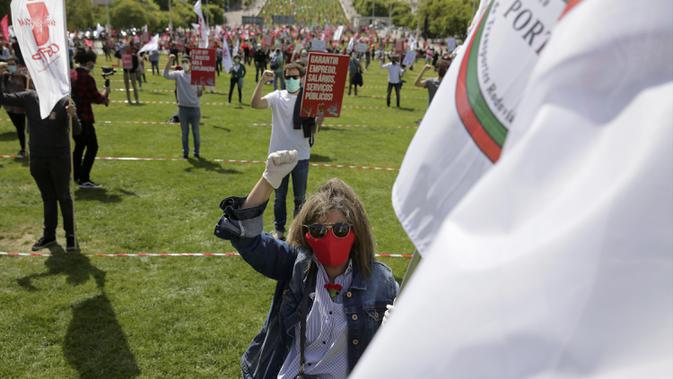 Seorang wanita memegang bendera serikat pekerja transportasi dan mengenakan masker saat memperingati Hari Buruh di tengah pandemi COVID-19 di Lisbon, Portugal, Jumat (1/5/2020). Aksi ini sudah mendapat persetujuan Kementerian Kesehatan dan Dalam Negeri Portugal. (AP Photo/Armando Franca)