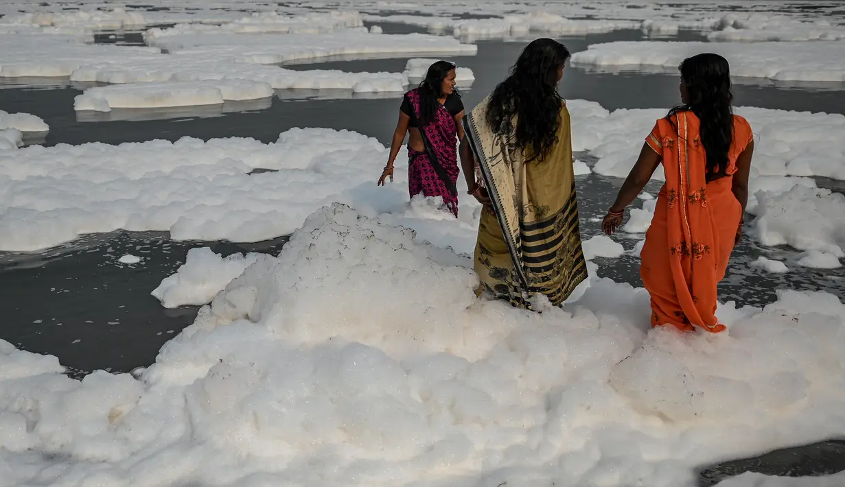Sejumlah wanita mandi di sungai Yamuna yang tertutup busa limbah sebagai bagian dari ritual untuk festival Chhath Puja yang akan datang di New Delhi, Senin (8/11/2021). Sungai yang sangat dianggap suci oleh umat Hindu India ini dipenuhi lapisan busa karena limbah beracun. (Sajjad HUSSAIN / AFP)