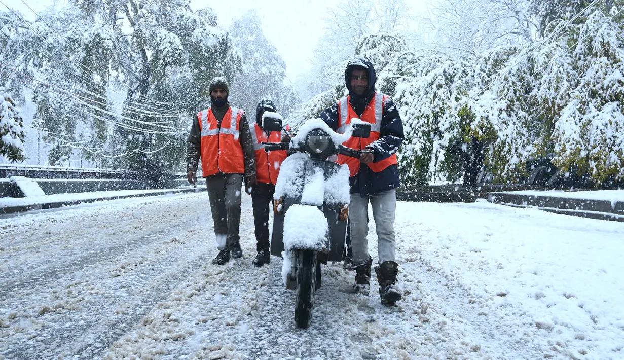 Pekerja mendorong skuter melintasi jalan yang tertutup salju di kota utama Kashmir, Srinagar, Kamis (7/11/2019). Srinagar menyambut salju pertama musim ini yang mulai turun. (Photo by Tauseef MUSTAFA / AFP)