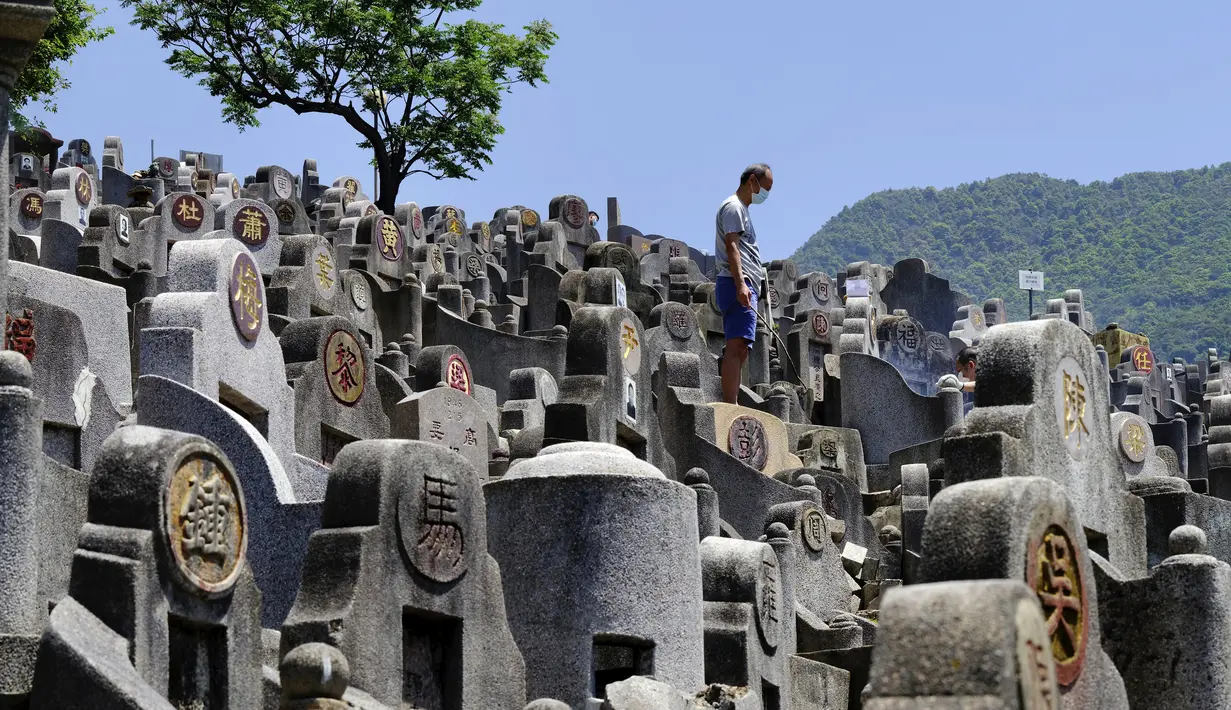 Seorang pria yang mengenakan masker berdiri di makam kerabat saat Festival Ching Ming atau Hari Sapu Makam di Hong Kong, Selasa (5/4/2022). Ribuan warga Hong Kong memberi hormat kepada leluhur dan kerabat mereka selama festival tahunan ini. (AP Photo/Vincent Yu)