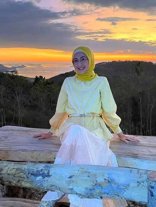 Menikmati sunset di NTT, Desy tampil stylish dengan padu padan striped blouse, rok, dan hijab kuning.
