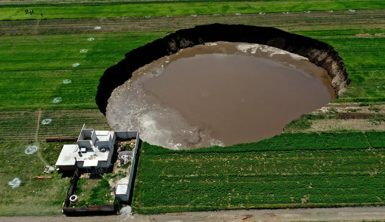Pemandangan udara dari sinkhole yang ditemukan oleh petani di lahan pertanian di Santa Maria Zacatepec, negara bagian Puebla, Meksiko, Senin (1/6/2021). Warga tiap hari khawatir karena sinkhole terus membesar dan mengancam menelan rumah mereka. (JOSE CASTAÑARES/AFP)