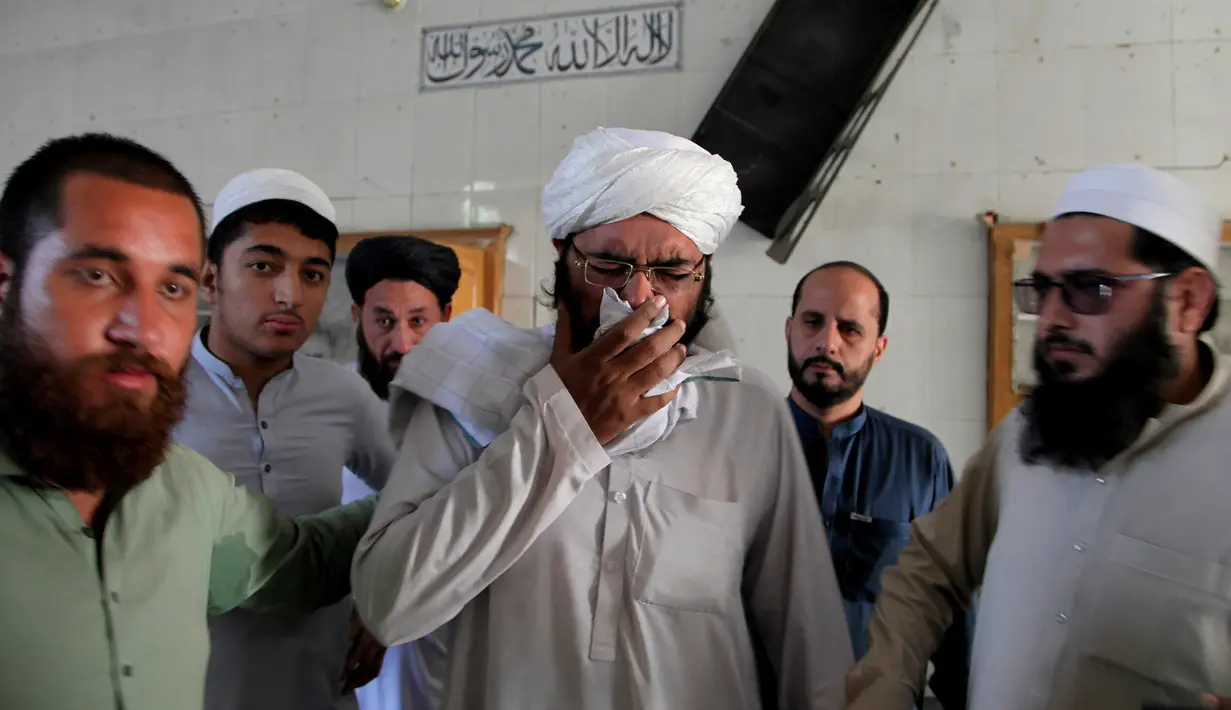 Orang-orang menenangkan seorang ulama yang kehilangan murid-muridnya di lokasi ledakan bom di sebuah madrasah di kota Peshawar, Pakistan, Selasa (27/10/2020). Lebih dari 60 orang sedang ada di ruang salah satu kelas saat itu, ketika ledakan mengguncang pada Selasa pagi. (AP Photo/Muhammad Sajjad)