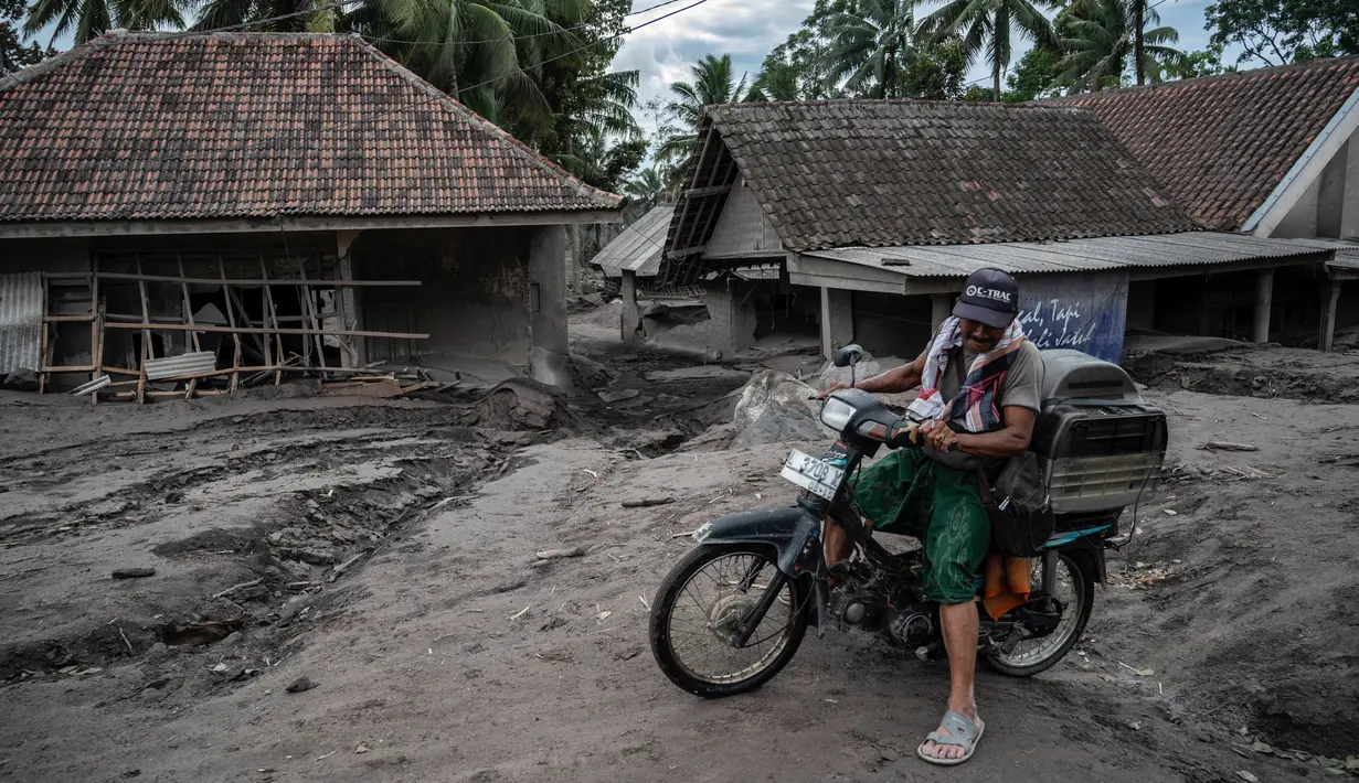 Seorang pria mengendarai sepeda melewati rumah yang rusak akibat erupsi Gunung Semeru di Desa Sumber Wuluh, Lumajang, Jawa Timur, Senin (6/12/2021). Desa Sumber Wuluh luluh lantak diterjang erupsi Semeru mengakibatkan puluhan rumah rusak dan ratusan warga mengungsi. (Juni Kriswanto/AFP)