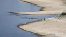 Seorang warga berjalan di Sungai Rhine dengan air yang rendah di Cologne, Jerman, Rabu (10/8/2022). Ketinggian air yang rendah mengancam industri Jerman karena semakin banyak kapal yang tidak dapat melintasi jalur air utama. Kekeringan yang parah akan memburuk di Eropa pada bulan Agustus karena musim panas yang panas dan kering terus berlanjut. (AP Photo/Martin Meissner)