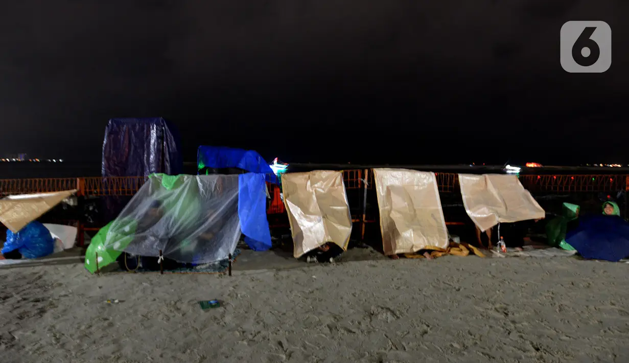 Pengunjung mendirikan tenda darurat untuk menikmati malam pergantian tahun di Kawasan Pantai Lagoon, Taman Impian Jaya Ancol, Jakarta, Selasa (31/12/2019). Meski Jakarta diguyur hujan sejak Selasa (31/12) sore, warga tetap antusias menikmati malam pergantian tahun. (merdeka.com/Imam Buhori)