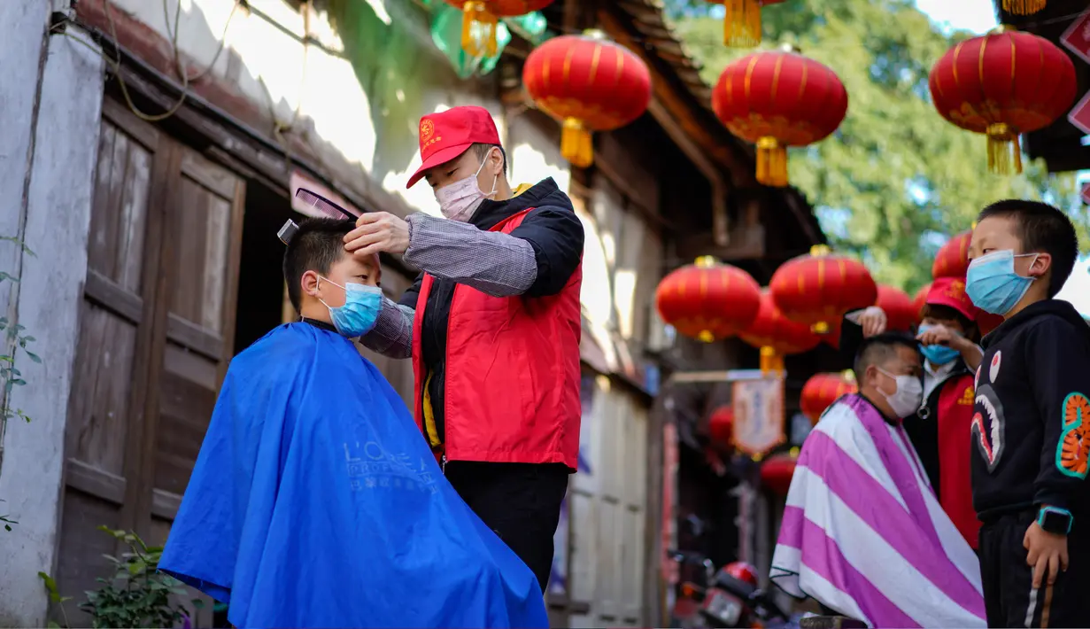 Seorang barber sukarelawan memotong rambut seorang anak laki-laki di sebuah permukiman di Kota Chongqing, China, pada 16 Februari 2020. Sejak merebaknya virus corona COVID-19, sebagian besar tempat potong rambut telah ditutup. (Xinhua/Liu Chan)