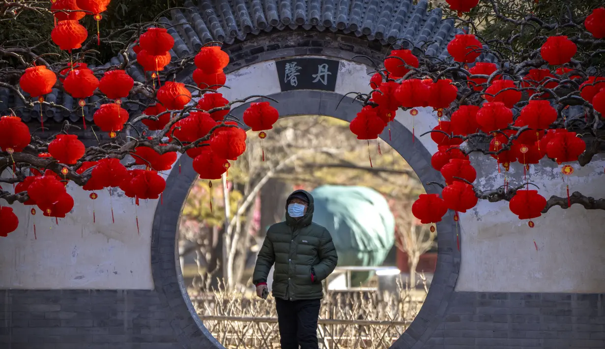 Seorang pria yang mengenakan masker berjalan melewati pepohonan yang dihiasi lentera untuk Tahun Baru Imlek di sebuah taman umum di Beijing, Jumat, 20 Januari 2023. Tahun Kelinci secara resmi dimulai pada 22 Januari. (AP Photo/Mark Schiefelbein)