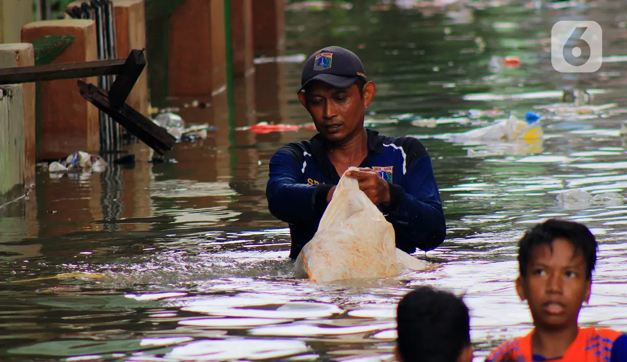 Petugas Sudin Sumber Daya Air (SDA) memunguti sampah-sampah yang tergenang saat banjir di kawasan Kampung Melayu Kecil, Bukit Duri, Jakarta, Selasa (25/2/2020). Banjir tersebut akibat luapan sungai Ciliwung. (merdeka.com/magang/ Muhammad Fayyadh)