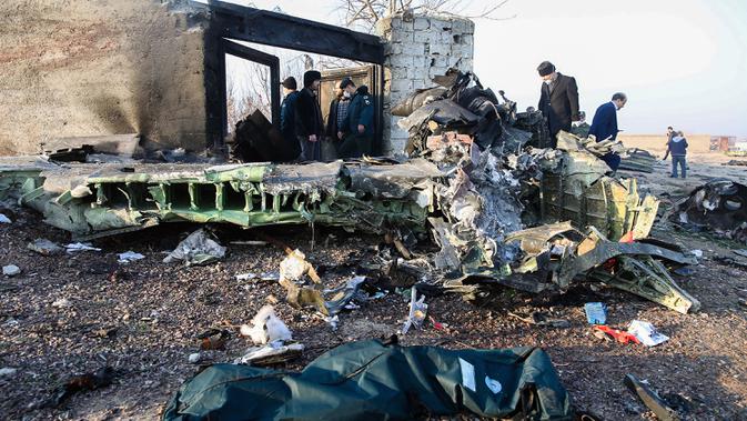 Orang-orang berdiri di antara puing-puing setelah pesawat Boeing 737 jatuh di dekat Bandara Internasional, Teheran, Iran, Rabu (8/1/2020). Seluruh penumpang pesawat maskapai Ukraina yang membawa 176 orang termasuk kru tersebut dilaporkan tewas. (ROHHOLLAH VADATI / ISNA / AFP)