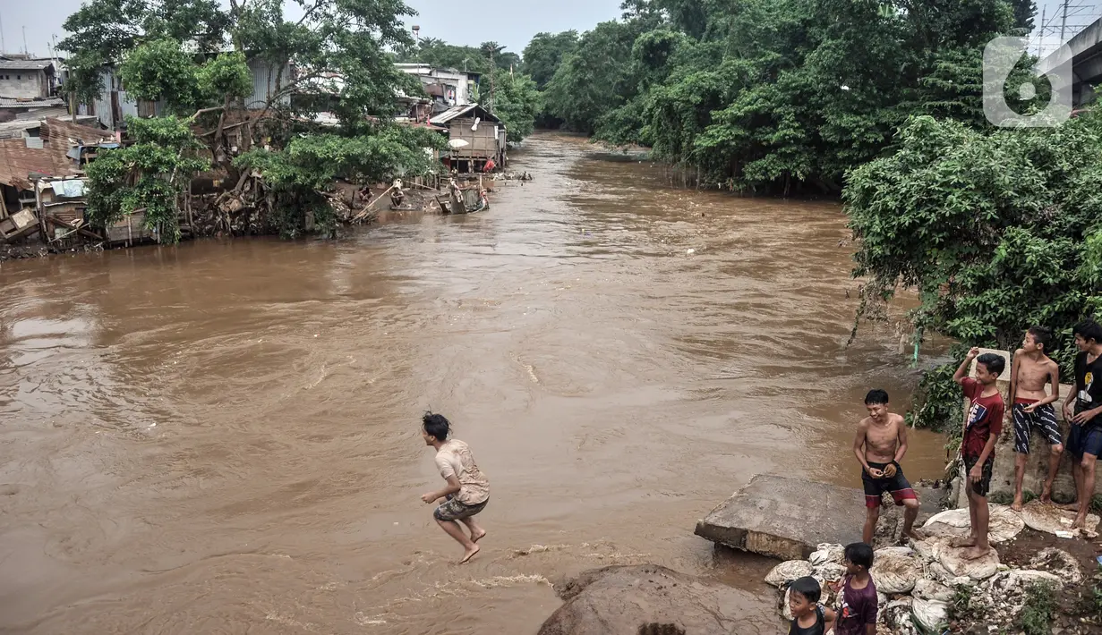 Seorang anak melompat ke Kali Ciliwung yang meluap, Kebon Pala, Jatinegara, Jakarta Timur, Minggu (31/10/2021). Aliran Kali Ciliwung yang meluap akibat hujan di kawasan hulu dimanfaatkan anak-anak untuk berenang meski membahayakan keselamatan. (merdeka.com/Iqbal S. Nugroho)