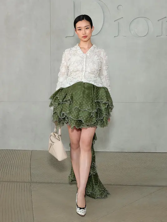 Yumi Kawai tampil dengan atasan putih lengan panjang bermotif dipadukan rok ruffle asimteris hijau bermotif. Artis Jepang ini juga membawa tas Dior warna beige dan mengenakan heels polkadot. [Dok. DIOR]
