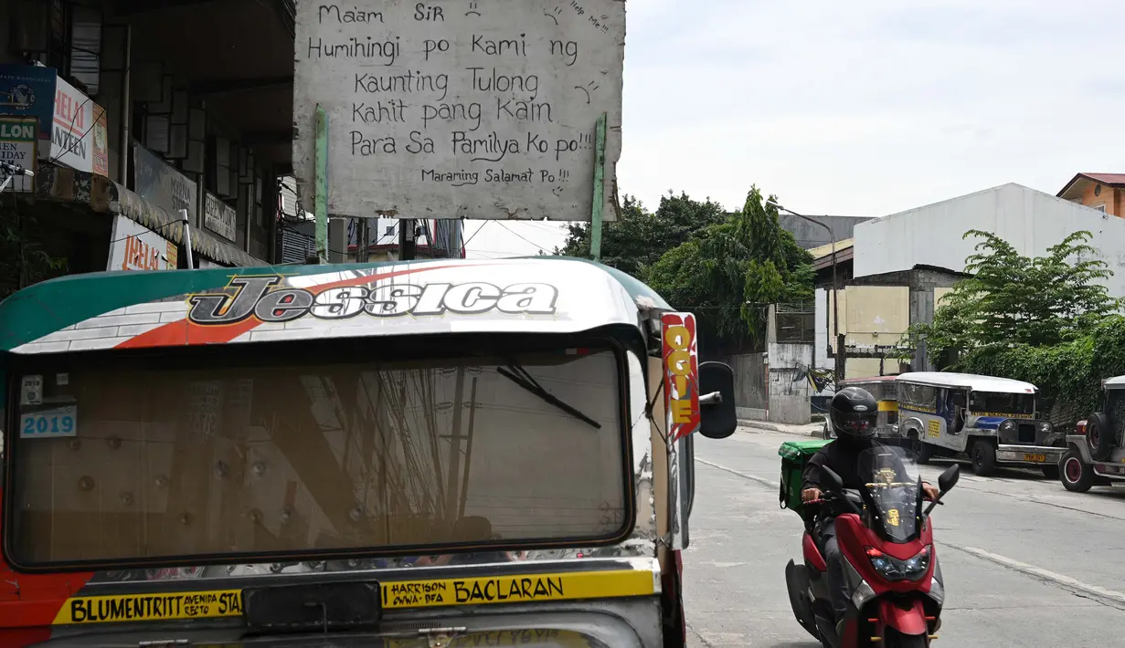 Pengendara motor melewati jeepney milik Daniel Flores yang berfungsi sebagai rumah sementara yang diparkir di Manila, 12 Agustus 2020. Angkutan ikonik di Filipina itu belum dapat mengangkut penumpang sejak Maret akibat lockdown Covid-19 yang membuat jutaan orang kehilangan pekerjaan (Ted ALJIBE/AFP)