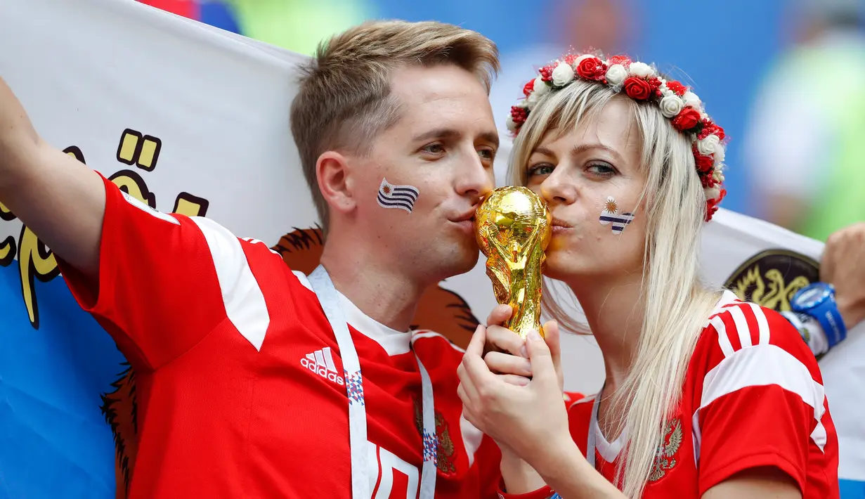 Pasangan Rusia mencium replika trofi Piala Dunia 2018 menjelang pertandingan Grup A antara Uruguay dan Rusia di Samara Arena, Samara, Rusia, Senin (25/6). (AP Photo/Rebecca Blackwell)