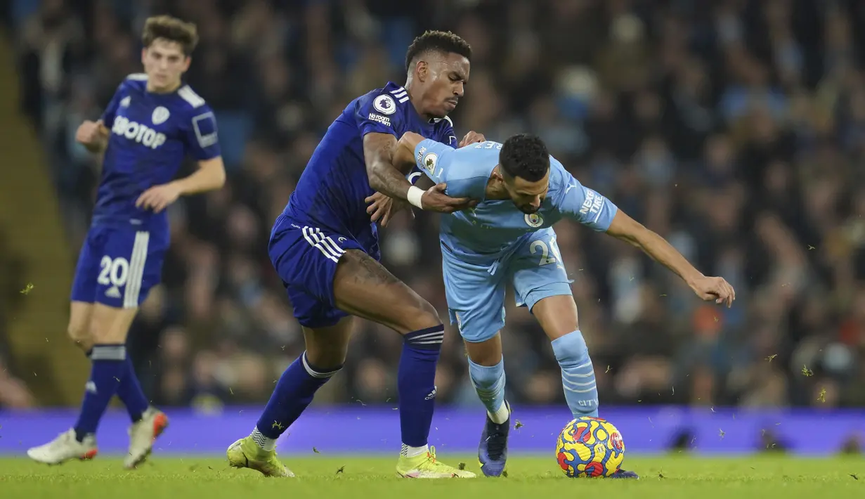 Penyerang Manchester City Riyad Mahrez berebut bola dengan bek Leeds United Junior Firpo dalam laga pekan ke-17 Liga Inggris di Etihad Stadium, Rabu (15/12/2021) dini hari WIB. Manchester City mencukur tamunya Leeds United tujuh gol tanpa balas. (AP Photo/Jon Super)