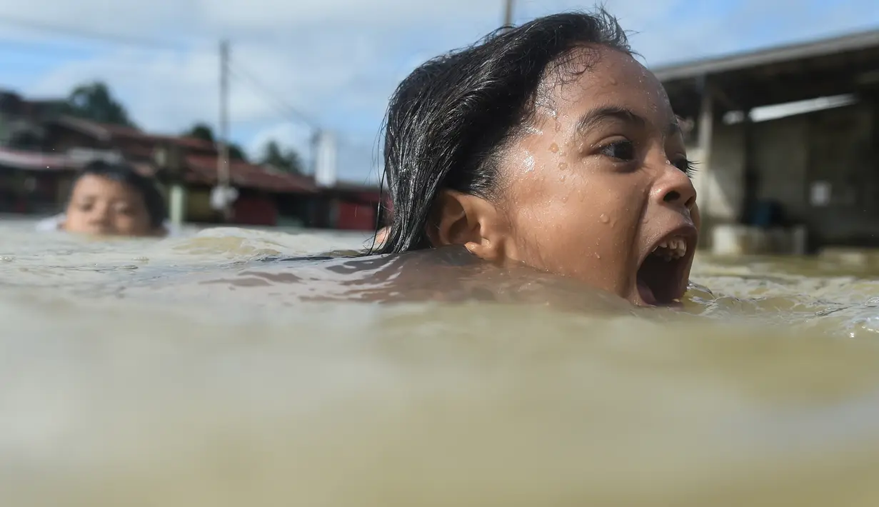 Anak-anak berenang saat banjir melanda kawasan Rantau Panjang, Malaysia, Kamis (5/1). Sekitar 23 ribu orang terpaksa mengungsi karena banjir yang disebabkan hujan muson ini. (AFP PHOTO / MOHD RASFAN)