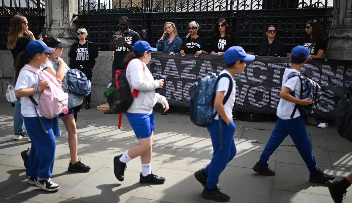 Anak-anak sekolah berjalan melewati aksi protes yang dilakukan oleh organisasi non-pemerintah Choose Love Europe di luar Gedung Parlemen di London, Inggris pada 29 Mei 2025. (Justin TALLIS/AFP)