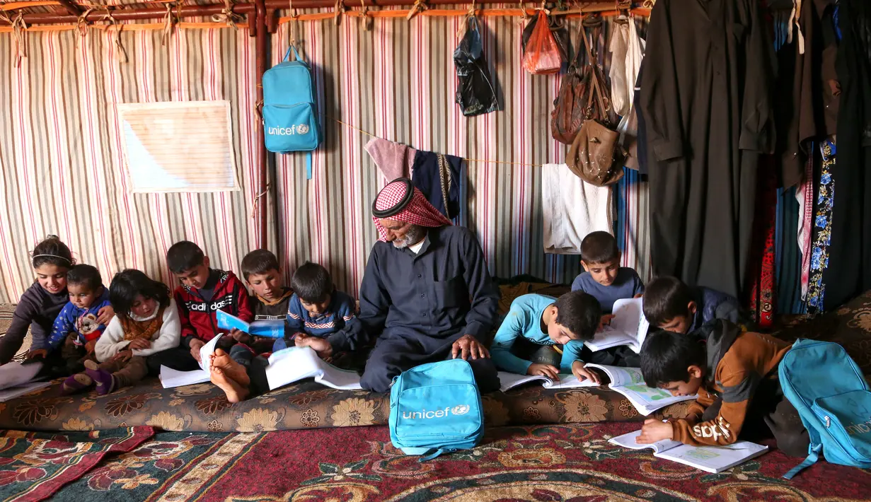 Abderrazaq Khatoun membantu tugas sekolah 11 cucunya di dalam tenda di desa Harbanoush, Suriah, 11 Maret 2021. Mengungsi dari rumah asalnya di provinsi Hama, Khatoun dan 30 anggota keluarga yang masih hidup mendirikan empat tenda di sebidang tanah yang dikelilingi pohon zaitun. (Ahmad al-ATRASH/AFP)
