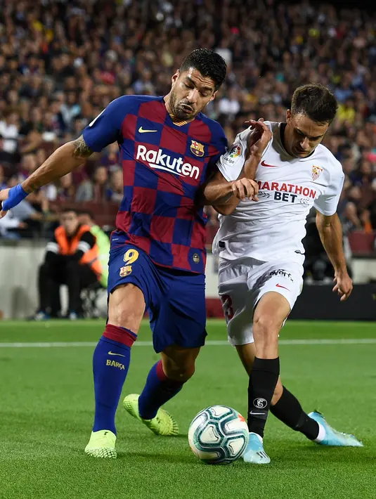 Penyerang Barcelona, Luis Suarez berebut bola dengan bek Sevilla Sergio Reguilon dalam pertandingan pekan kedelapan kompetisi La Liga Spanyol 2019-2020 di Camp Nou, Minggu (6/10/2019). Barcelona berhasil menang telak atas Sevilla dengan skor 4-0. (Josep LAGO / AFP)