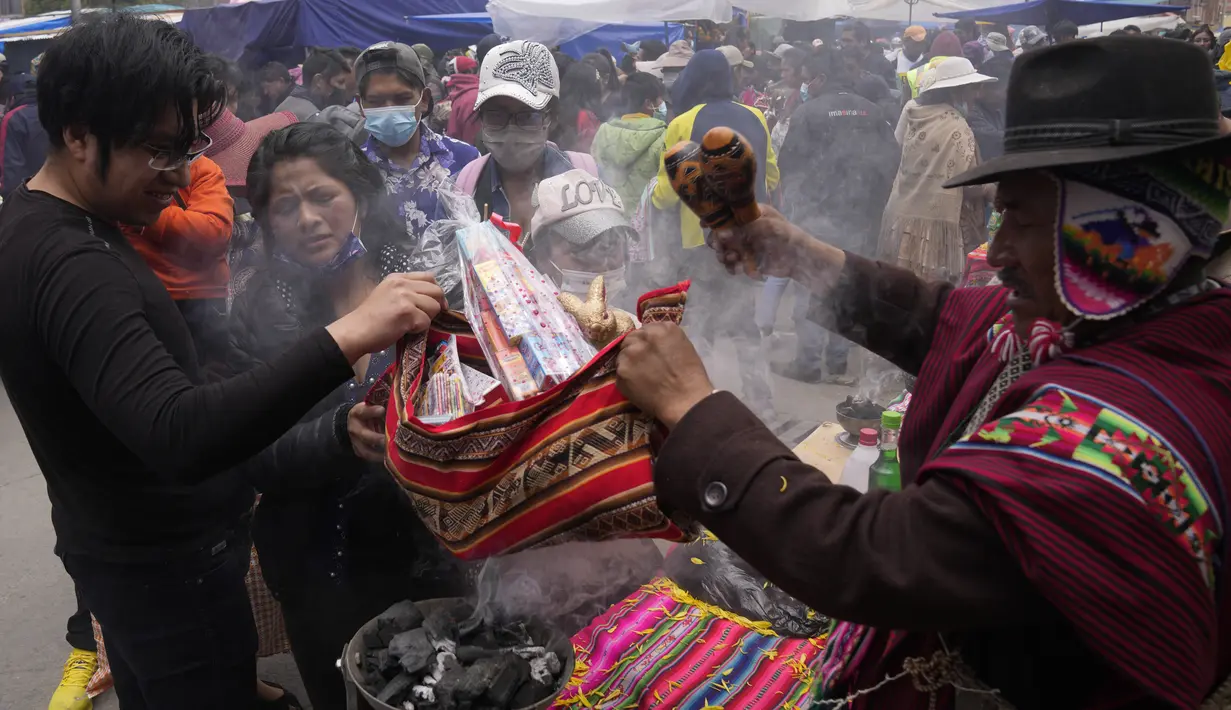 Seorang cenayang memberkati miniatur rumah dan uang palsu untuk seorang klien pada hari pembukaan Alasita Fair tahunan di El Alto, Bolivia, Selasa (24/1/2023). Barang- barang yang telah dibeli tidak dibawa pulang begitu saja. Ada cenayang yang mendoakan barang-barang tersebut dengan dupa dan bubuk khusus. (AP Photo/Juan Karita)