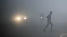 Seorang pria menyeberang jalan ketika kendaraan menembus kabut suhu dingin di New Delhi, Senin (30/12/2019). New Delhi, ibu kota India, saat ini mengalami musim dingin dengan hari dingin terpanjang dalam 22 tahun terakhir. (Photo by Jewel SAMAD / AFP)