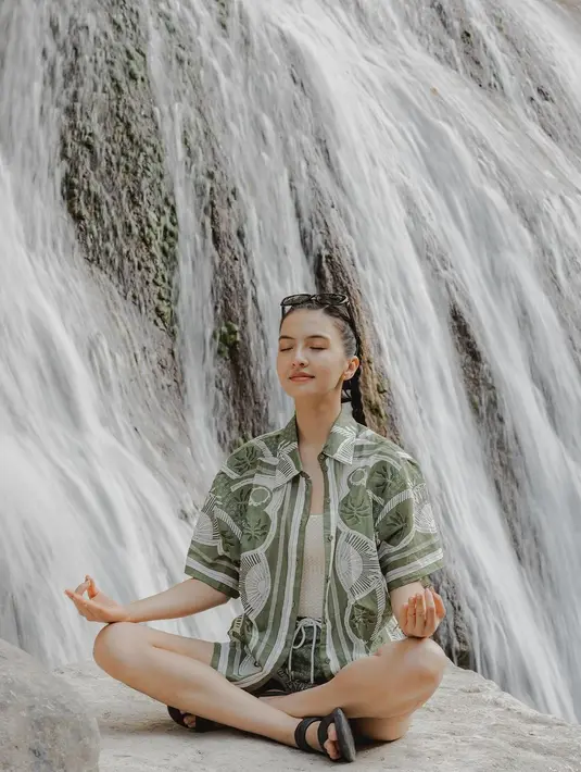 Menemukan kedamaian di air terjun, Raline Shah tampil nyaman dengan busana santai. Ia kenakan setelan loose shirt dan celana pendek hijau dengan knitwear sebagai inner. [@ralineshah]