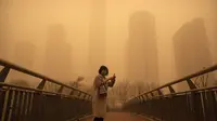 Seorang perempuan berjalan di sepanjang jembatan penyeberangan di tengah badai pasir pada jam sibuk pagi hari di kawasan pusat bisnis di Beijing, China, Senin (15/3/2021). Kota Beijing diselimuti debu cokelat tebal, Senin pagi, yang dibawa angin kencang dari Mongolia. (AP Photo/Mark Schiefelbein)
