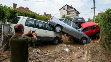 Warga mengambil gambar mobil yang rusak akibat banjir bandang di Ibu Kota Skopje, Makedonia, Minggu (7/8). Pemerintah menyatakan keadaan darurat sehari setelah setidaknya 21 orang tewas dalam banjir bandang yang disebabkan badai. (Robert ATANASOVSKI/AFP)