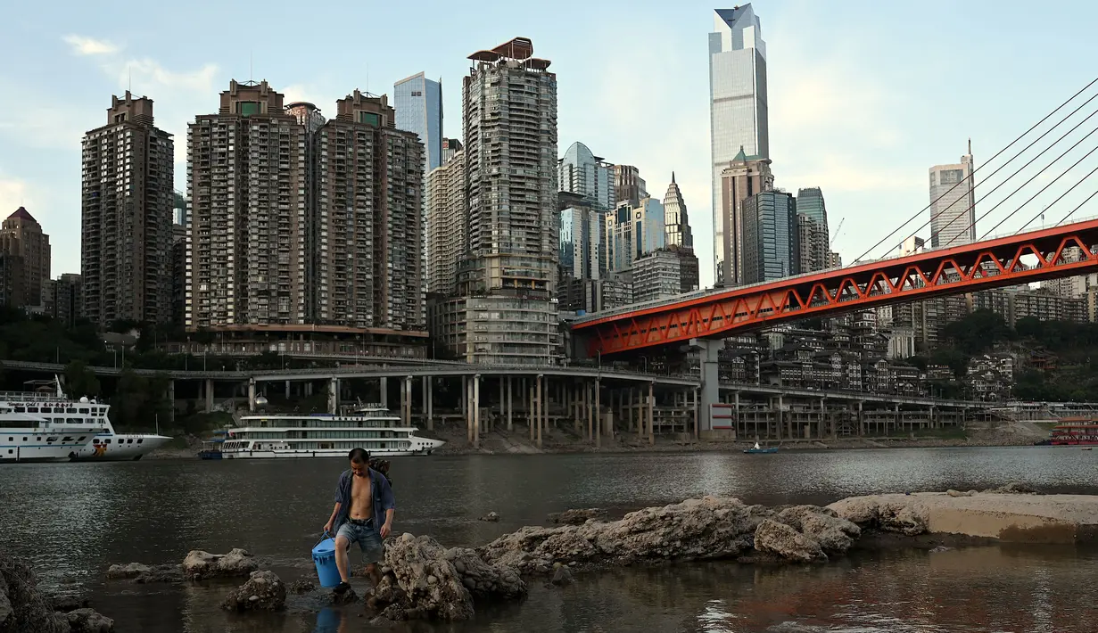 Seorang pemancing mengarungi air setelah memancing di Sungai Jialing, anak Sungai Yangtze, di Kota Chongqing, China, Rabu (24/8/2022). Sungai Yangtze telah mencapai level air terendah, dengan seluruh bagian dan lusinan anak sungai mengering. (Noel Celis/AFP)