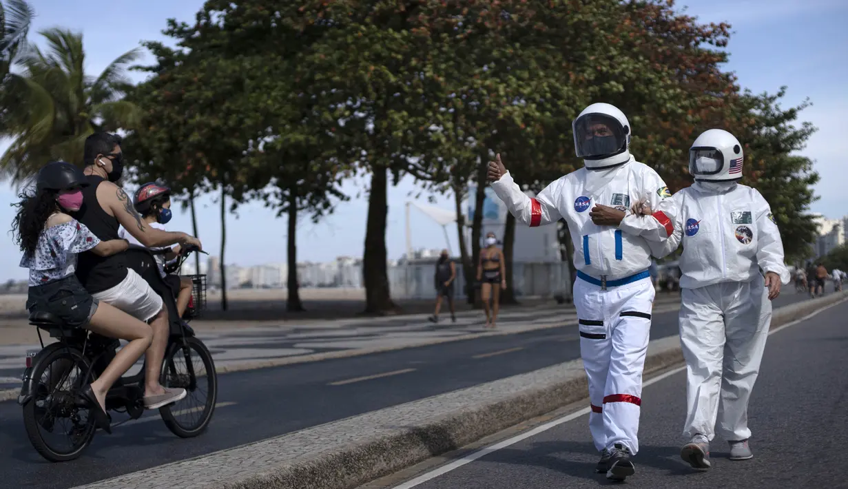 Akuntan Brasil Tercio Galdino (66) memberi isyarat jempol kepada warga yang mengendarai sepeda motor saat dia dan istrinya Alicea Galdino berjalan di sepanjang pantai Leme dengan pakaian pelindung mirip astronaut, Rio de Janeiro, Brasil, 12 Juli 2020. (Mauro Pimentel/AFP)