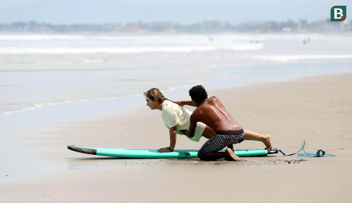 Seorang pendamping memberikan pelatihan dasar berselancar untuk para wisatawan atau pemula di Pantai Seminyak, Bali. (Bola.com/M iqbal Ichsan)