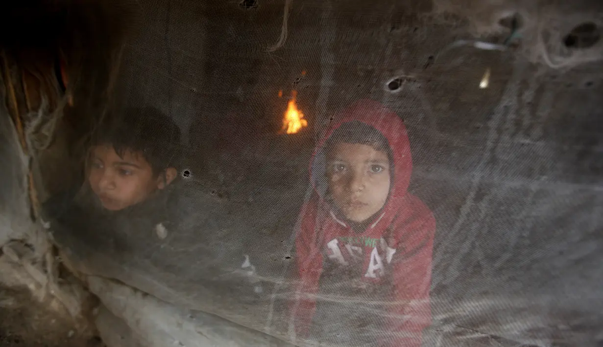 Anak-anak pengungsi Suriah melihat melalui jendela tenda saat mencoba tetap hangat di kamp pengungsi dekat Zahrani, Lebanon, 19 Januari 2022. Beberapa membakar pakaian tua, plastik, dan bahan berbahaya lainnya agar tetap hangat saat suhu turun dan kemiskinan melonjak. (AP Photo/Mohammed Zaatari)