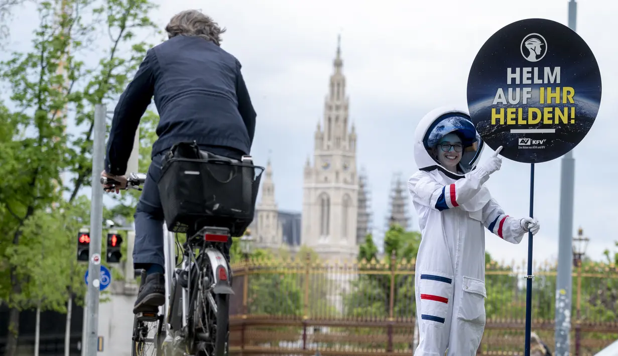 Seorang siswa berkostum astronaut memperlihatkan peringatan kepada pengendara sepeda untuk mengenakan helm di Ring Street, Austria, Rabu (5/5/2021). Delapan siswa Wina berpartisipasi dalam acara tersebut untuk mengingatkan pengendara sepeda mengenakannya helm demi keamanan mereka. (JOE KLAMAR/AFP)