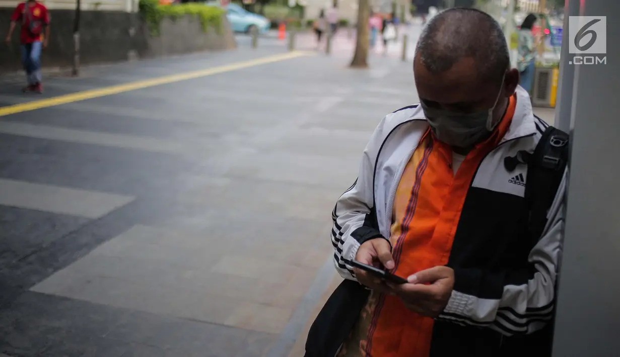 Seorang pria memakai masker pelindung  sambil bermain ponsel di Jakarta, Rabu (17/7/2019). Dinkes DKI menyarankan masyarakat untuk menggunakan masker saat beraktivitas untuk mencegah dampak polusi udara pada tubuh. (Liputan6.com/Faizal Fanani)