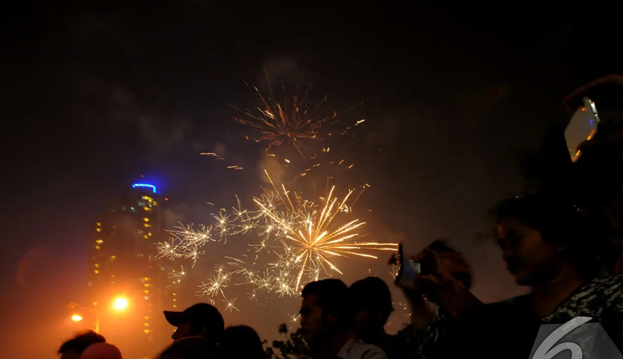 Sejumlah pengunjung mengabadikan warna-warni kembang api di langit Ancol, Jakarta, Kamis (1/1/2015). (Liputan6.com/Faisal R Syam)