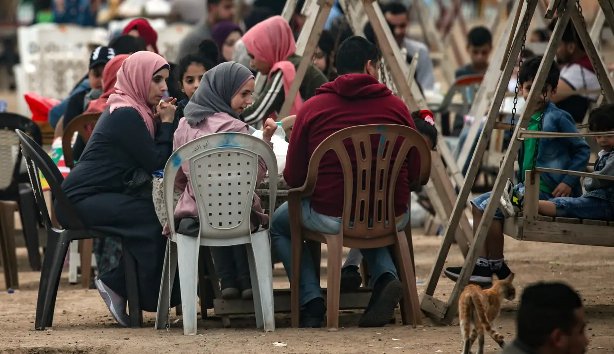 Warga Palestina berkumpul untuk berbagi makanan buka puasa selama bulan suci Ramadan, saat pandemi virus corona, di sepanjang pantai kota Gaza pada 13 Mei 2020. Mereka menunggu waktu berbuka puasa sambil menyaksikan matahari terbenam. (Photo by MAHMUD HAMS / AFP)