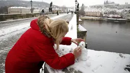 Seorang wanita membangun manusia salju di Jembatan Charles abad pertengahan setelah hujan salju pertama di Praha, Republik Ceko (3/12/2020). (AP Photo / Petr David Josek)