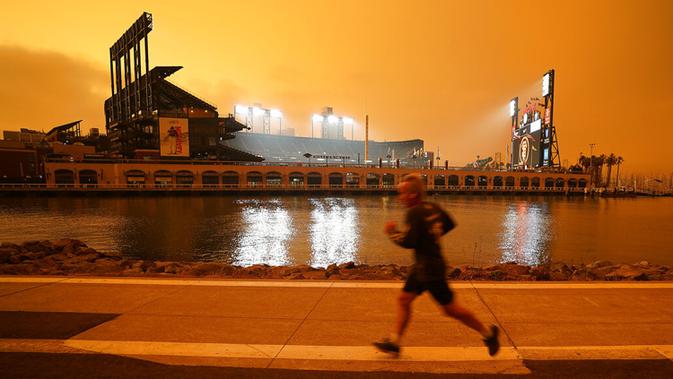 Seorang pria berlari di sepanjang McCovey Cove saat kabut asap menyelimuti langit di luar Oracle Park, San Francisco, Amerika Serikat, Rabu (9/9/2020). Kebakaran hutan di seluruh Barat mengakibatkan langit San Francisco hingga Seattle berwarna oranye yang menakutkan. (AP Photo/Tony Avelar)