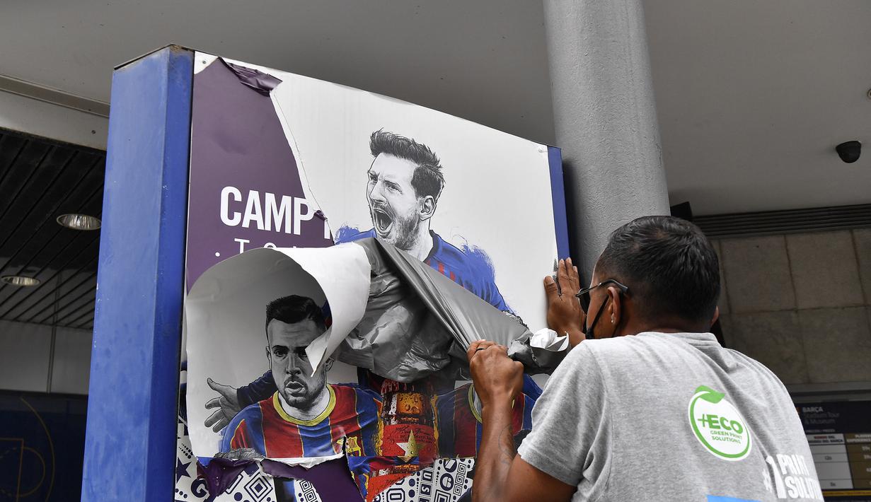 Seorang pekerja melepas poster-poster yang menampilkan pemain depan Barcelona Lionel Messi di stadion Camp Nou di Barcelona (10/8/2021). Prancis menunggu dengan tidak sabar Lionel Messi dengan para pendukung berkumpul di luar lapangan Paris Saint-Germain. (AFP/ Pau Barrena)