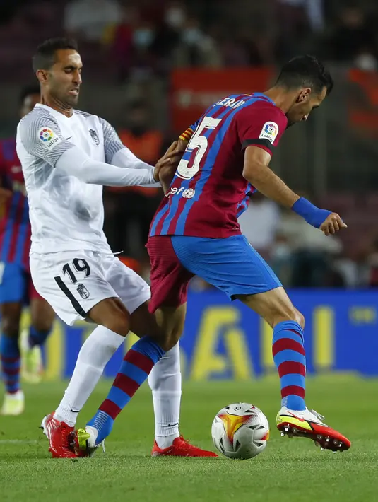 Gelandang Granada, Angel Montoro berebut bola dengan gelandang Barcelona, Sergio Busquets pada lanjutan La Liga di Camp Nou, Selasa (21/9/2021) dini hari WIB. Barcelona dipaksa bermain imbang 1-1 oleh tamunya Granada. (AP Photo/Joan Monfort)