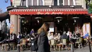 Seorang perempuan mengenakan masker, berjalan di depan kafe Paris yang terbuka, di Paris, Senin (14/3/2022). Prancis telah mencabut sebagian besar pembatasan COVID-19 pada hari Senin, memungkinkan orang melepas masker di hampir semua tempat. (AP Photo/Francois Mori)