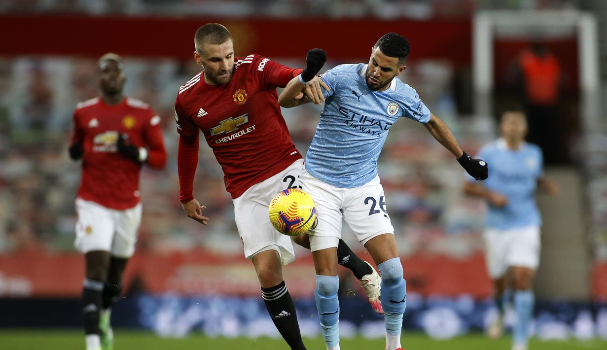 Bek Manchester United, Luke Shaw (kiri), berebut bola dengan striker Manchester City, Riyad Mahrez, dalam laga lanjutan Liga Inggris 2020/21 pekan ke-12 di Old Trafford Stadium, Sabtu (12/12/2020). Manchester United bermain imbang 0-0 dengan Manchester City. (AFP/Phil Noble/Pool)