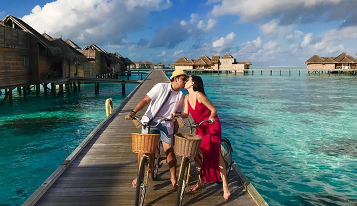 Foto di jembatan pinggir pantai itu keduanya tampak santai saat sedang di atas sepeda cium bibir. Dibelakang, tampak beberapa penginapan yang berdiri di atas laut biru. Suasana begitu romantis keduanya terlihat berciuman.  (Instagram/sammysimorangkir)