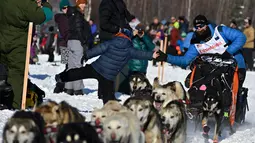 Dallas Seavey membungkuk untuk melakukan high-five saat Iditarod Sled Dog Race di Deshka Landing di Willow, Alaska, Minggu (7/3/2021). Jarak yang harus ditempuh biasanya hampir 1.000 mil dan tahun ini dikurangi menjadi sekitar 100 mil. (Marc Lester/Anchorage Daily News via AP)