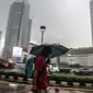 Warga menggunakan payung melintas di kawasan Bundaran Hi, Jakarta, Sabtu (13/11/2021). Badan Meteorologi Klimatologi dan Geofisika (BMKG) melansir peringatan terbaru yang berlaku 7-9 November 2021 soal peringatan cuaca ekstrem imbas dari La Nina. (Liputan6.com/Faizal Fanani)