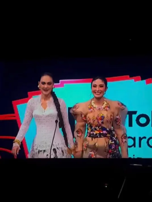 Ayu Dewi mengenakan busana berpotongan kebaya dengan siluet bahu yang tegas dan bervolume dari Mel Ahyar. Sentuhan motif bunga memberi kesan playful. [@lunamaya]